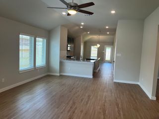 An open living area with wood floors, modern lighting, and large windows next to a sleek kitchen featuring granite countertops.