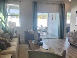 A stylish living room with soft-toned furnishings, wood flooring, and large windows leading to an inviting outdoor patio.