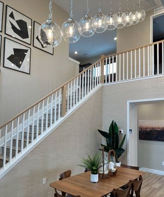 A modern interior with a sleek staircase, artistic wall decor, and a wooden dining table beneath stylish pendant lights.