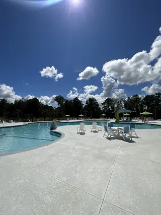 A sunny community pool area with seating and umbrellas. Perfect for relaxation in Carolina Groves Townhomes by D.R. Horton (Moncks Corner, SC).