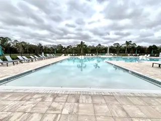 A luxurious pool with ample lounge chairs and palm trees in Naples Village at Verona I by KB Home (Titusville, FL).