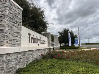 Street view Stone entrance sign amidst lush landscaping at Trinity Lakes by Landsea Homes in Groveland, FL.