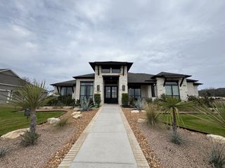 Street view A modern stone home with sleek black accents and a manicured desert landscape in Megan's Landing Half Acre by Perry Homes (San Antonio, TX).
