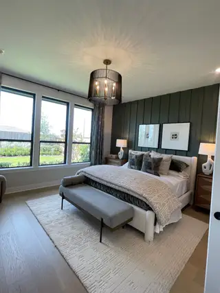 A serene bedroom with a cozy bed, textured accent wall, large windows, statement chandelier, and elegant decor.