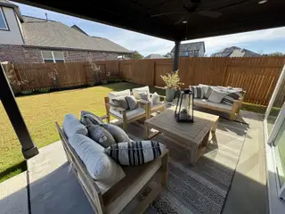 Model Home A cozy outdoor patio with plush seating, a wooden table, and lush lawn, perfect for relaxation and gatherings.
