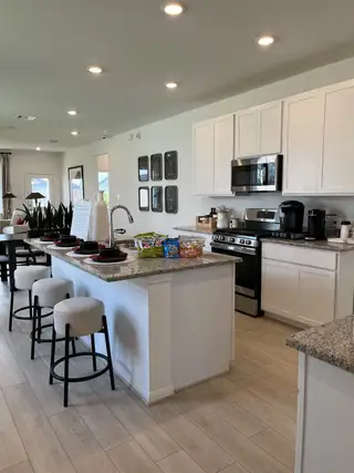 A modern kitchen with sleek white cabinets, granite countertops, an island with bar stools, and stainless steel appliances.