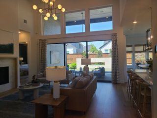 A bright, contemporary living area with high ceilings, modern lighting, and expansive windows overlooking a manicured backyard.