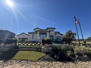 A beautifully landscaped home with a stone and stucco facade, featuring manicured gardens and decorative planters in Caliterra by Drees Custom Homes, Dripping Springs, TX.