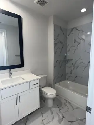 A sleek bathroom featuring marble-patterned tiles, a modern vanity, and a spacious bathtub.