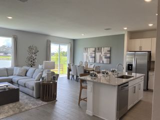 Model Home A modern, open-concept living space with a cozy sectional, sleek kitchen island, and dining area overlooking a tranquil view.