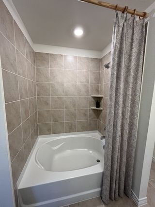 A stylish bathtub and shower combo featuring neutral beige tiles, built-in shelving, and a modern shower curtain for a fresh, inviting look.
