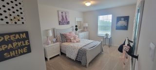 Model Home A charming bedroom with a white bed frame, pink accents, and whimsical artwork creates a playful and inviting space.