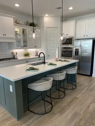 A stylish kitchen with white cabinetry, glass pendant lighting, and a striking green island.