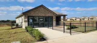 A model home in The Links at River Bend by D.R. Horton (Floresville, TX) with brick and siding exterior, featuring a black iron fence.