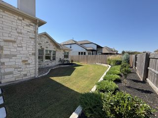 Street view A charming stone home with a manicured lawn and lush landscaping in Blackhawk by Scott Felder Homes (Pflugerville, TX).