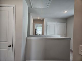 A bright hallway with soft grey walls, recessed lighting, and double doors, offering a spacious and modern feel.