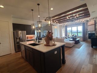 An elegant open-concept kitchen with pendant lights, dark cabinetry, and a cozy living area with large windows and chic decor.
