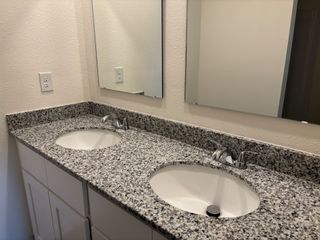 A modern bathroom featuring dual granite sinks, elegant fixtures, and sleek mirrors.