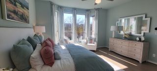 A bright primary bedroom with a bay window, soft blue walls, a plush bed, and a dresser creates a serene, light-filled space.