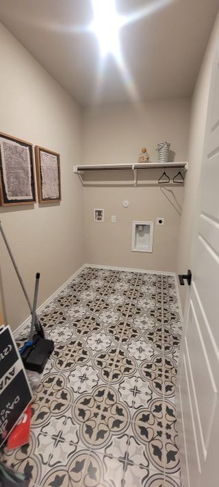 A functional laundry room with patterned tiles, wall art, shelving, and room for a washer and dryer.