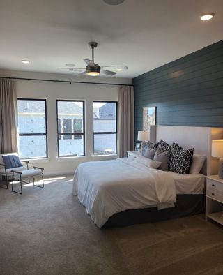 A modern bedroom with dark accent wall, light bedding, large windows, and a ceiling fan creating a cozy yet stylish ambiance.