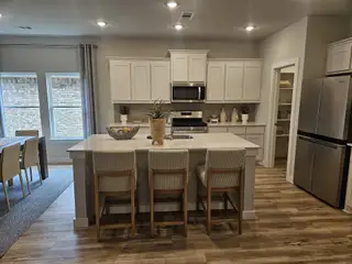 A modern kitchen with sleek white cabinetry, a spacious island, and cozy dining area, featuring elegant wooden flooring.