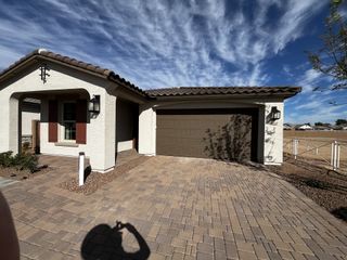 A Mediterranean-style house with brown shutters, a dark garage, and a paved driveway, set in a sunny neighborhood.
