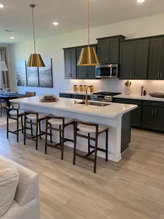 A modern kitchen featuring dark cabinetry, a spacious island with elegant seating, and chic gold pendant lighting.