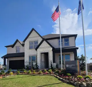 Street view A beautiful stone and brick home with lush landscaping in Painted Tree Woodland District 60 by Bloomfield Homes (McKinney, TX).