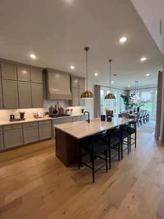 Model Home A modern kitchen with an island, warm lighting, sleek cabinetry, and a dining area with large windows for natural light.