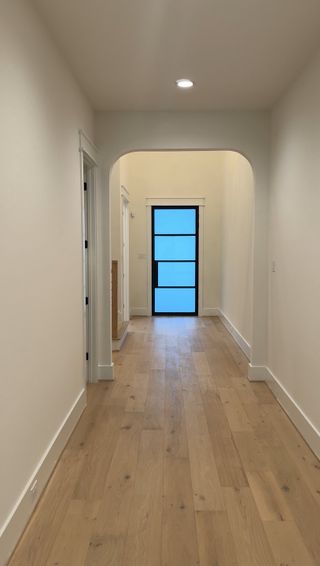 Model Home Hallway: A welcoming hallway with arched entryways, light wood flooring, and a contemporary glass-paneled front door.