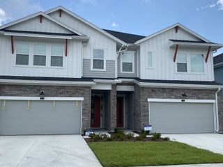 A charming modern duplex with gray stone, white siding, and lush lawn in Kettering at eTown - Paired Villas by David Weekley Homes (Jacksonville, FL).