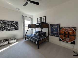 A contemporary bedroom featuring a black metal bunk bed with a plaid comforter, complemented by industrial-style artwork and a modern ceiling fan.