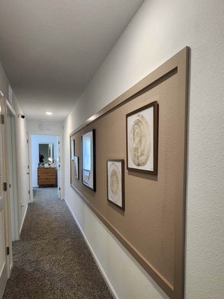 A carpeted hallway adorned with framed art and neutral tones, leading to a cozy bedroom, creating a warm, inviting atmosphere.