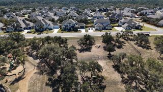 An aerial view showcasing the Caliterra community by Drees Custom Homes in Dripping Springs, TX, featuring spacious homes and natural landscapes interspersed with residential areas.