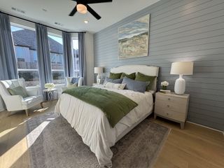 A serene bedroom with soft green accents, natural light, and a cozy sitting area perfect for unwinding.