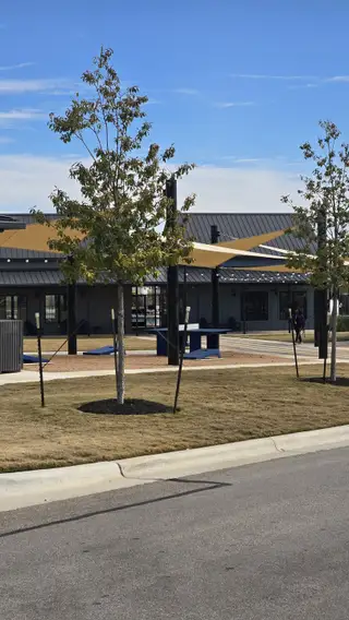 Community Amenities A beautifully designed clubhouse with shaded seating, a ping pong table, and contemporary landscaping in Harvest Ridge by Brohn Homes (Elgin, TX).