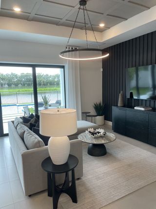 A modern living room with sleek furniture, large windows, and a chic pendant light, offering views of the outdoor landscape.