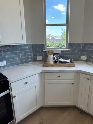 A bright kitchen corner featuring white cabinets, sleek countertops, and glossy blue tile backsplash with a scenic window view.