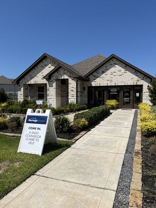 A charming beige brick home with lush landscaping in Massey Oaks - Estate Series by Meritage Homes (Pearland, TX).