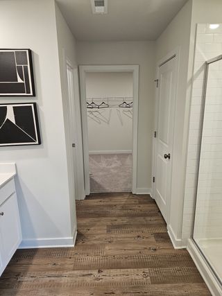 Model Home A bright bathroom with wood-look flooring, a walk-in closet, and a sleek glass shower.