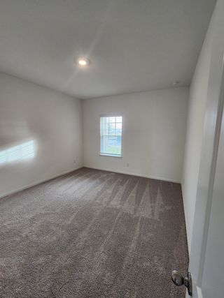 A spacious bedroom with plush carpet, white walls, and a bright window, offering a cozy and inviting atmosphere.