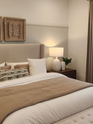 A cozy bedroom with a beige headboard, textured pillows, and warm lighting on a wooden nightstand.