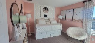 A cozy bedroom with pink walls, a plush chair, and elegant decor, featuring a daybed with ample pillows and stylish accents.