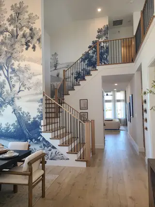 A modern interior with a striking staircase, blue landscape mural, and elegant dining area on wood flooring.