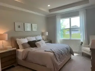 A cozy bedroom featuring a plush bed, soft lighting, and large window with sheer curtains.