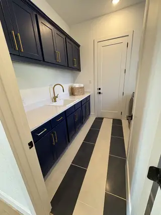 Model Home A sleek laundry room with navy cabinets, brass hardware, and a modern sink, featuring stylish striped tile flooring.