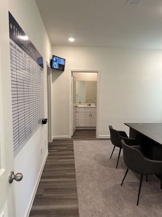 A modern office area with sleek flooring, a conference table, and a small wall-mounted screen leading to a tidy bathroom.