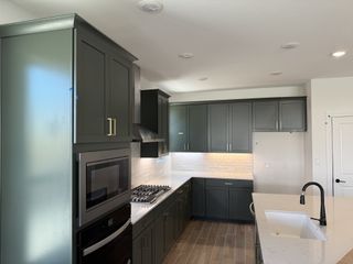 Model Home A stylish kitchen with dark green cabinetry, white quartz countertops, and stainless steel appliances.
