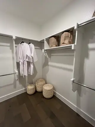A spacious walk-in closet featuring wooden floors, plush robes, and stylish woven storage baskets.